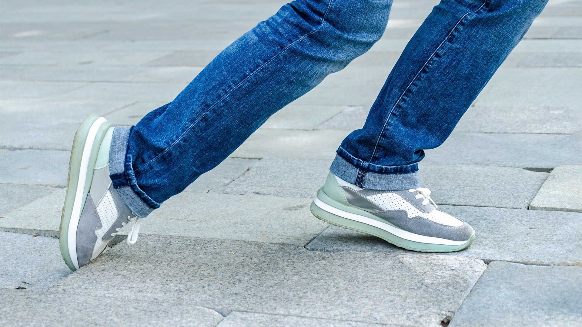 A person wearing jeans and sneakers is walking on a sidewalk.