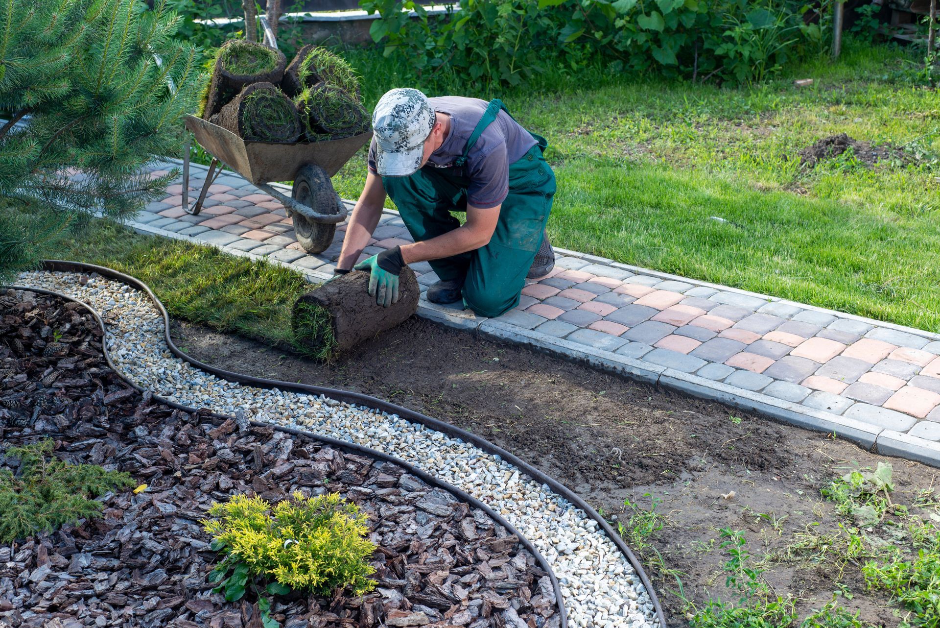 Close-up of gloved hands planting a small green seedling into dark garden soil under warm sunlight.