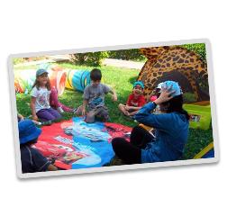 Un grupo de niños está sentado alrededor de una mujer jugando a las cartas.