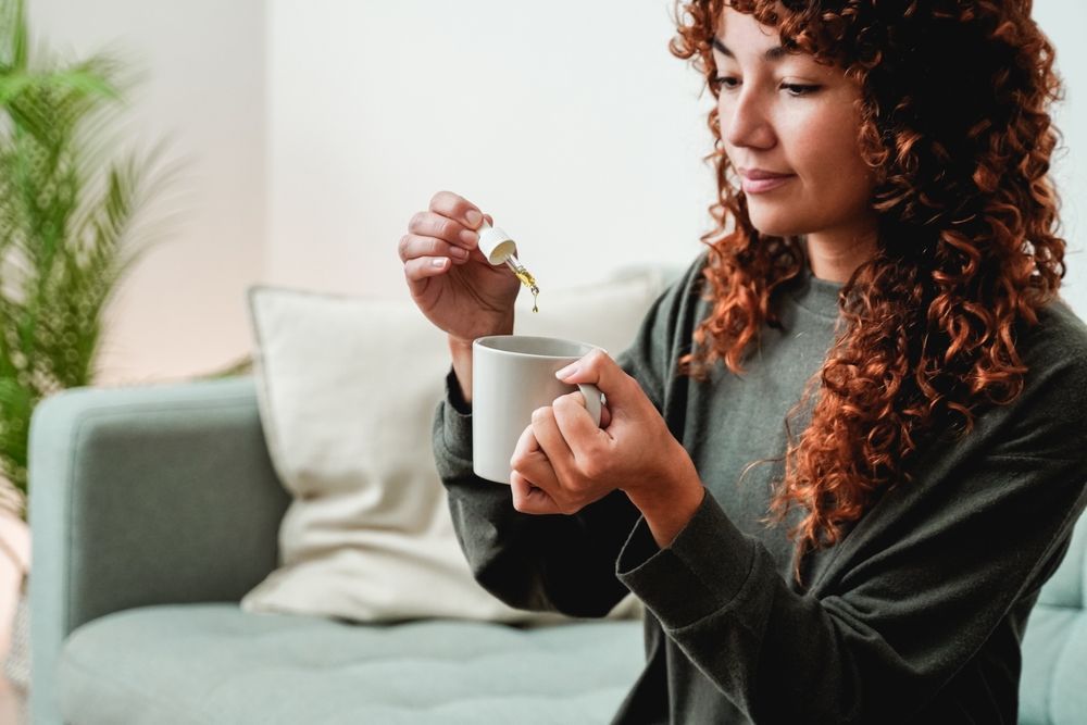 A woman is sitting on a couch drinking a cup of coffee.