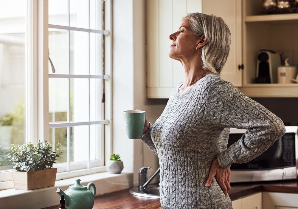 An older woman is standing in a kitchen holding a cup of coffee.