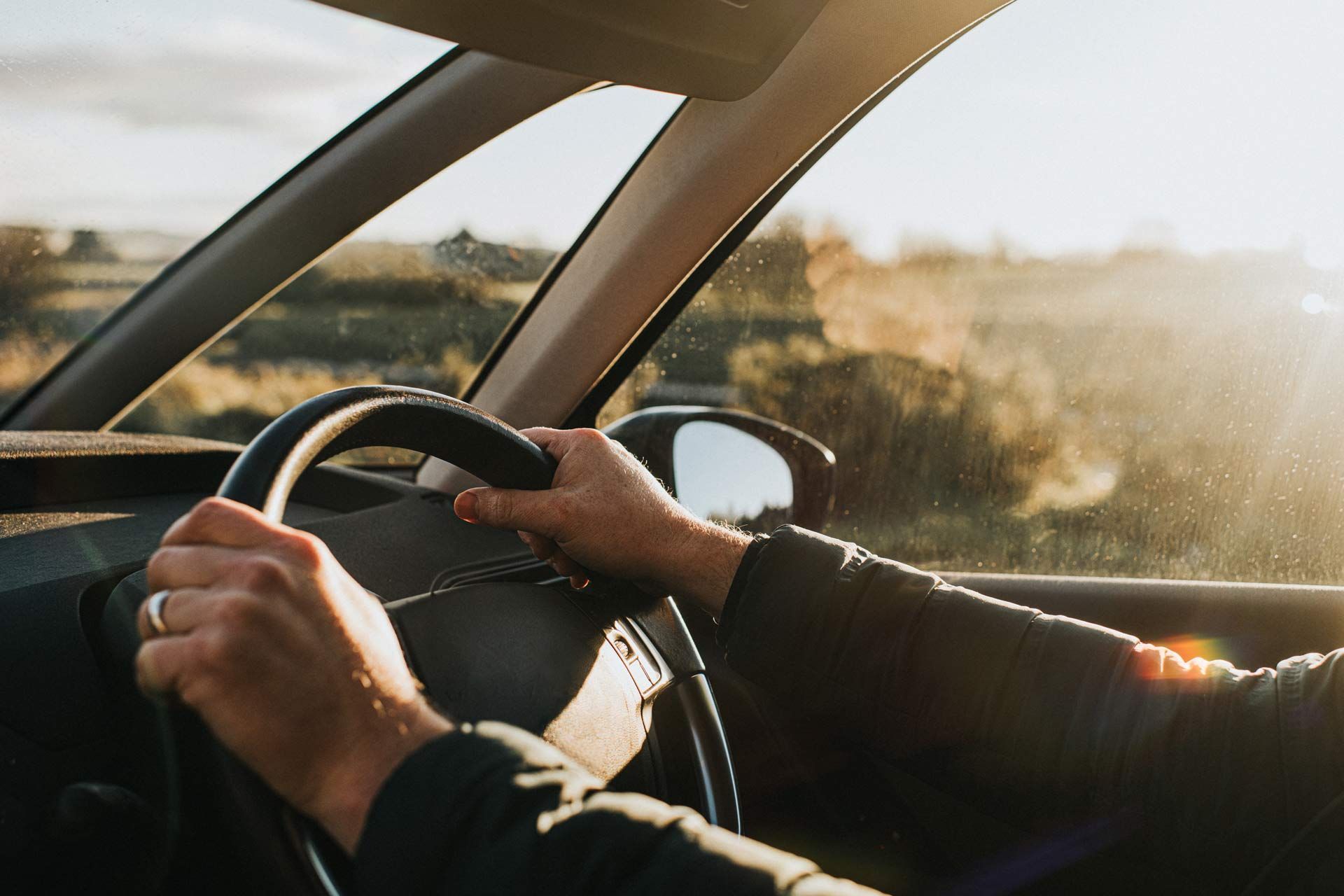 A pair of hands is holding a steering wheel in a car.
