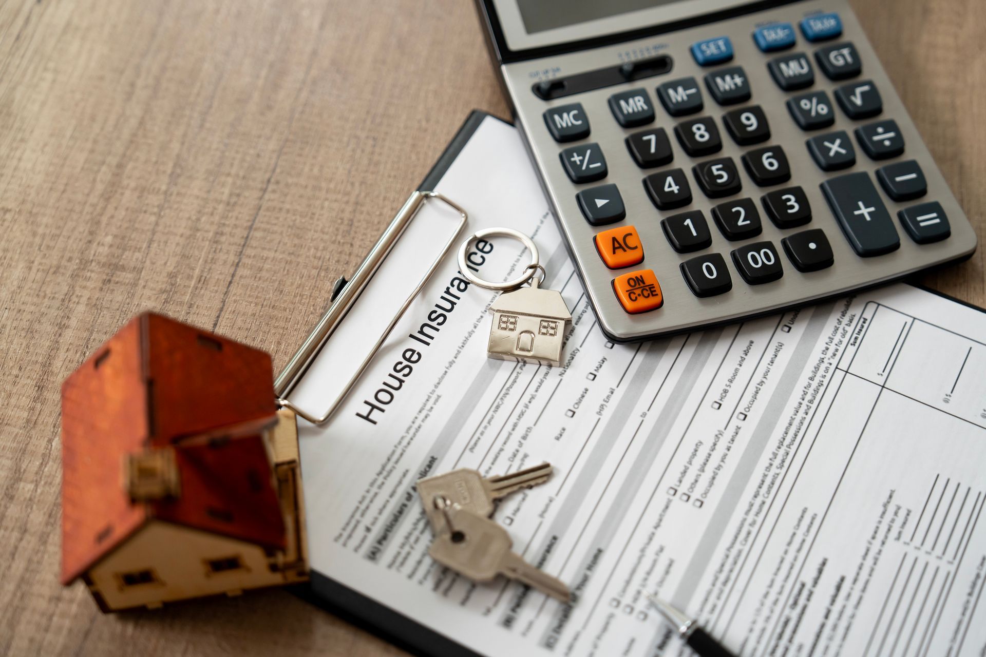 House insurance paperwork, a calculator, a toy house, and keys representing homeowners insurance.