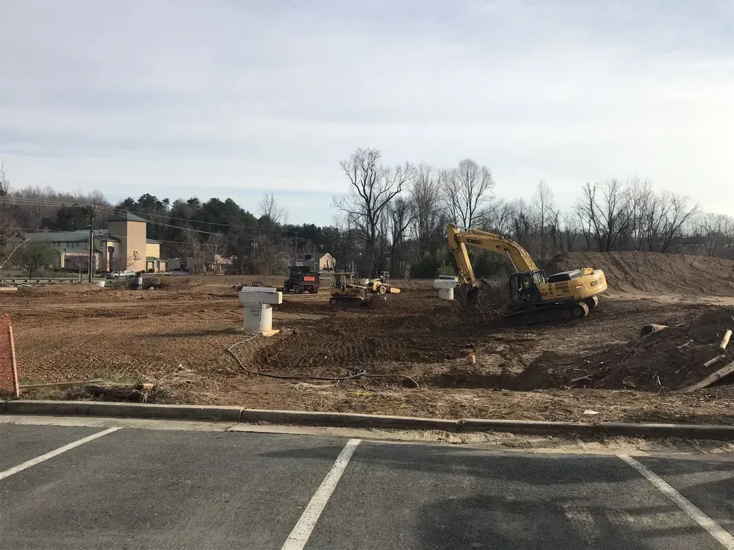 Construction site with excavator and bulldozer on a cleared lot, with a church in the background.