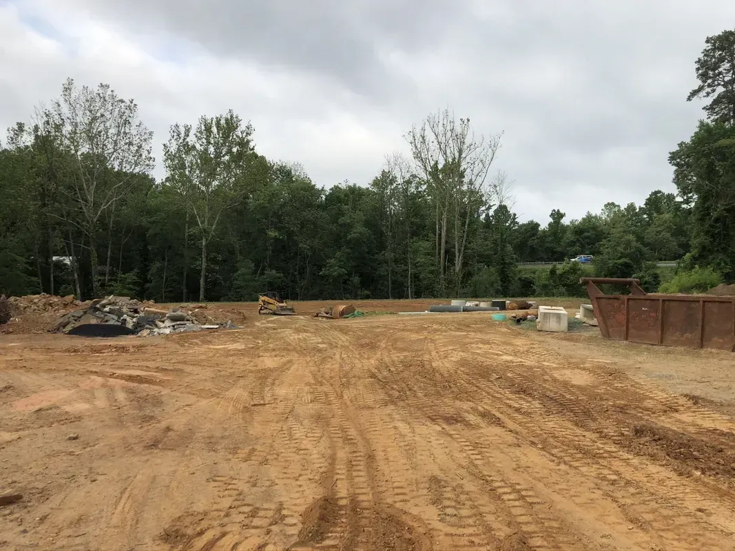Dirt lot, construction site with trees in the background, cloudy sky.
