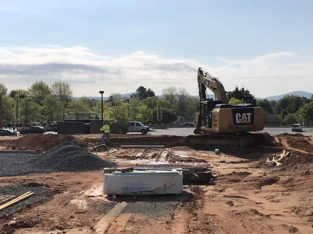 An excavator digs in a construction site with dirt and gravel under a bright sky.