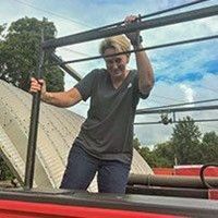 Woman in gray shirt, gripping a metal structure, smiling, outdoors.