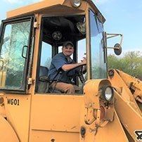 Man in a blue shirt operating a yellow construction vehicle.