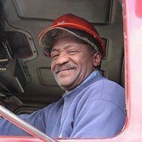 Truck driver in red hard hat smiles while driving.