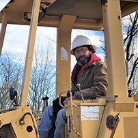 Man in hard hat operating heavy machinery in an outdoor setting.