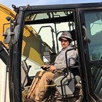 Man in hard hat operating machinery in a vehicle cab.