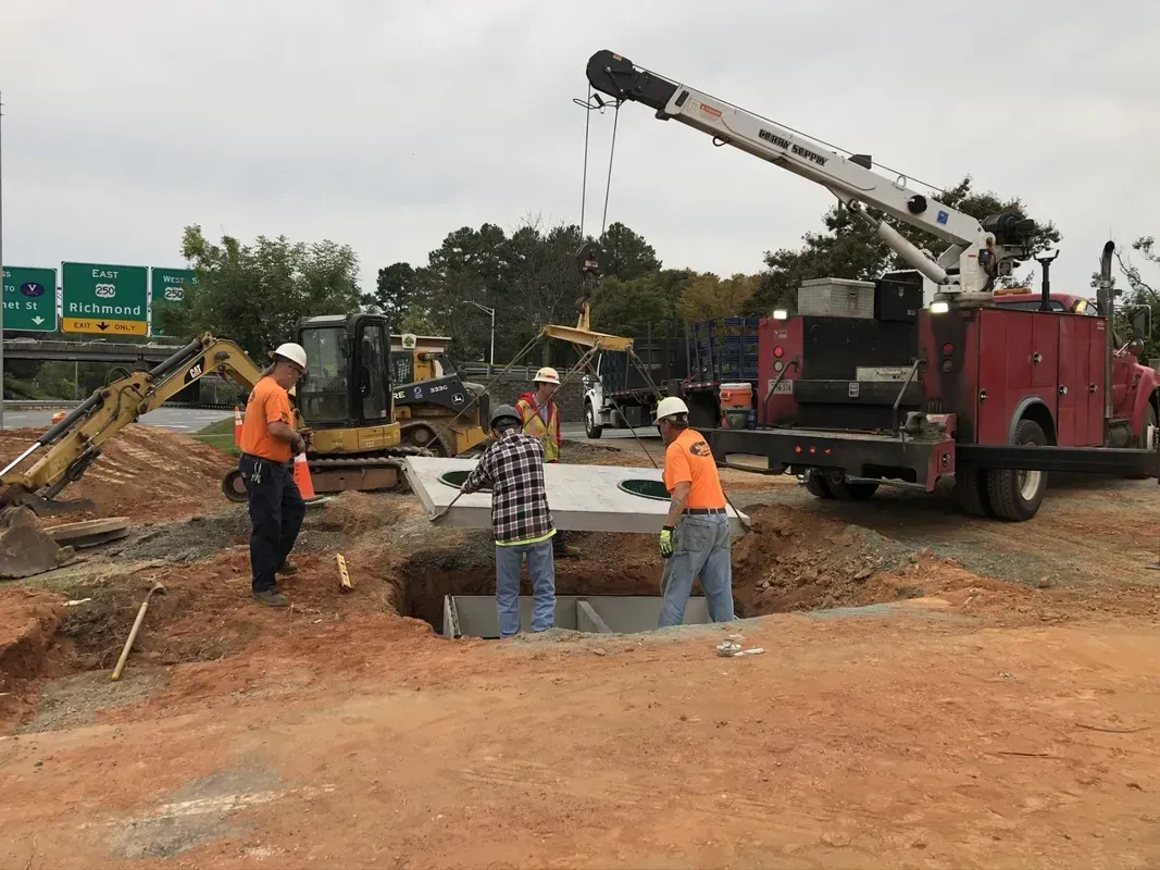 Construction workers install concrete structure with a crane, near a highway.