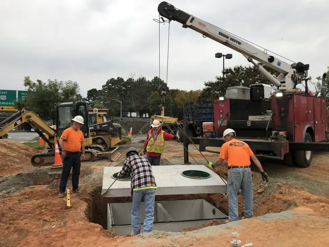 Construction workers installing a concrete structure with a crane. Men in orange shirts and hard hats working on site.