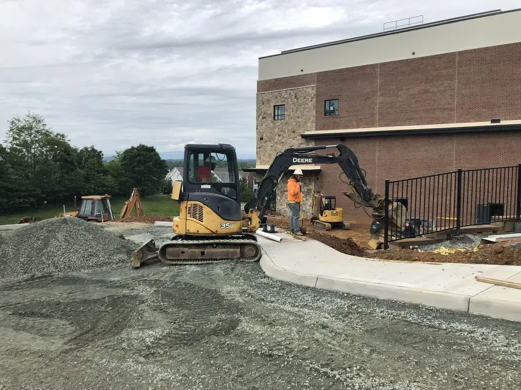 Construction site with an excavator and workers near a building with a brick facade.