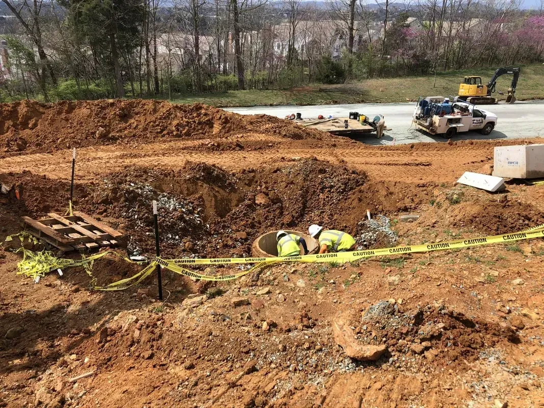 Construction site with exposed dirt and workers in safety vests. Yellow caution tape surrounds the area.