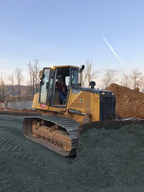 Yellow bulldozer pushing gravel on a construction site; operator inside, clear sky.