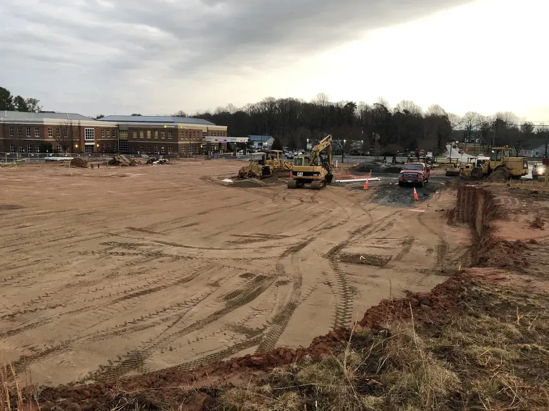 Construction site with heavy machinery, a building, and overcast sky.