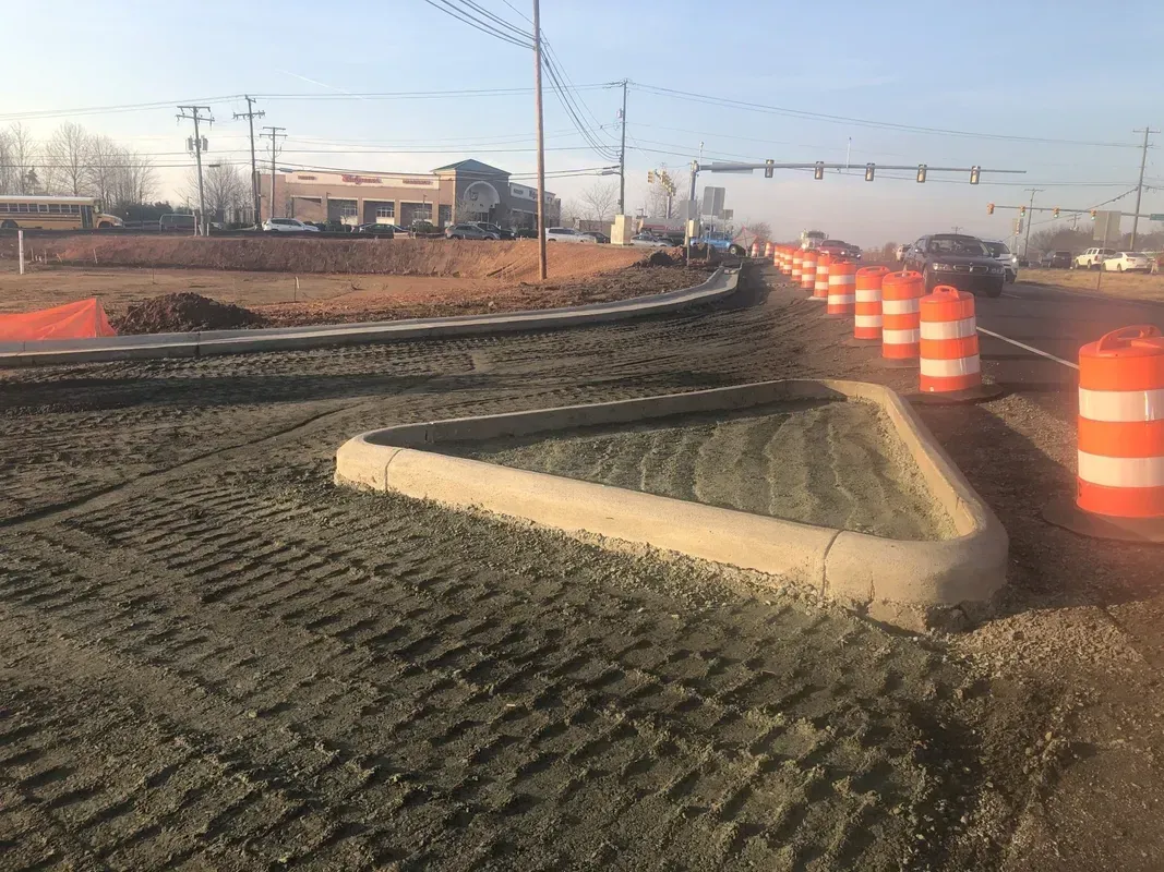 Road construction site with concrete curb, orange barrels, and a road under construction.