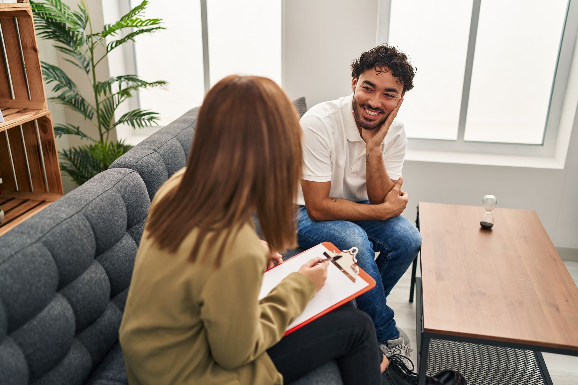 Two people talking in a bright office lounge, one taking notes on a clipboard.