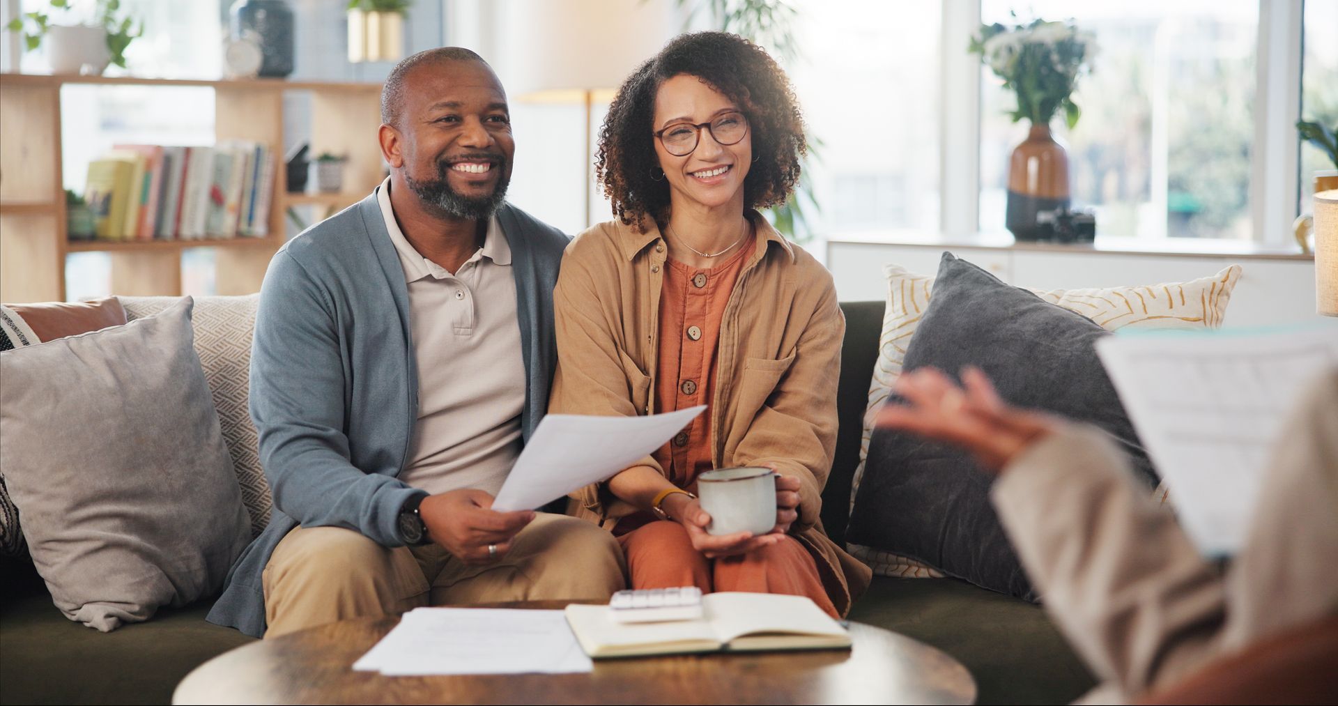 Two people smiling on a couch, reviewing papers in a bright living room with a coffee table.