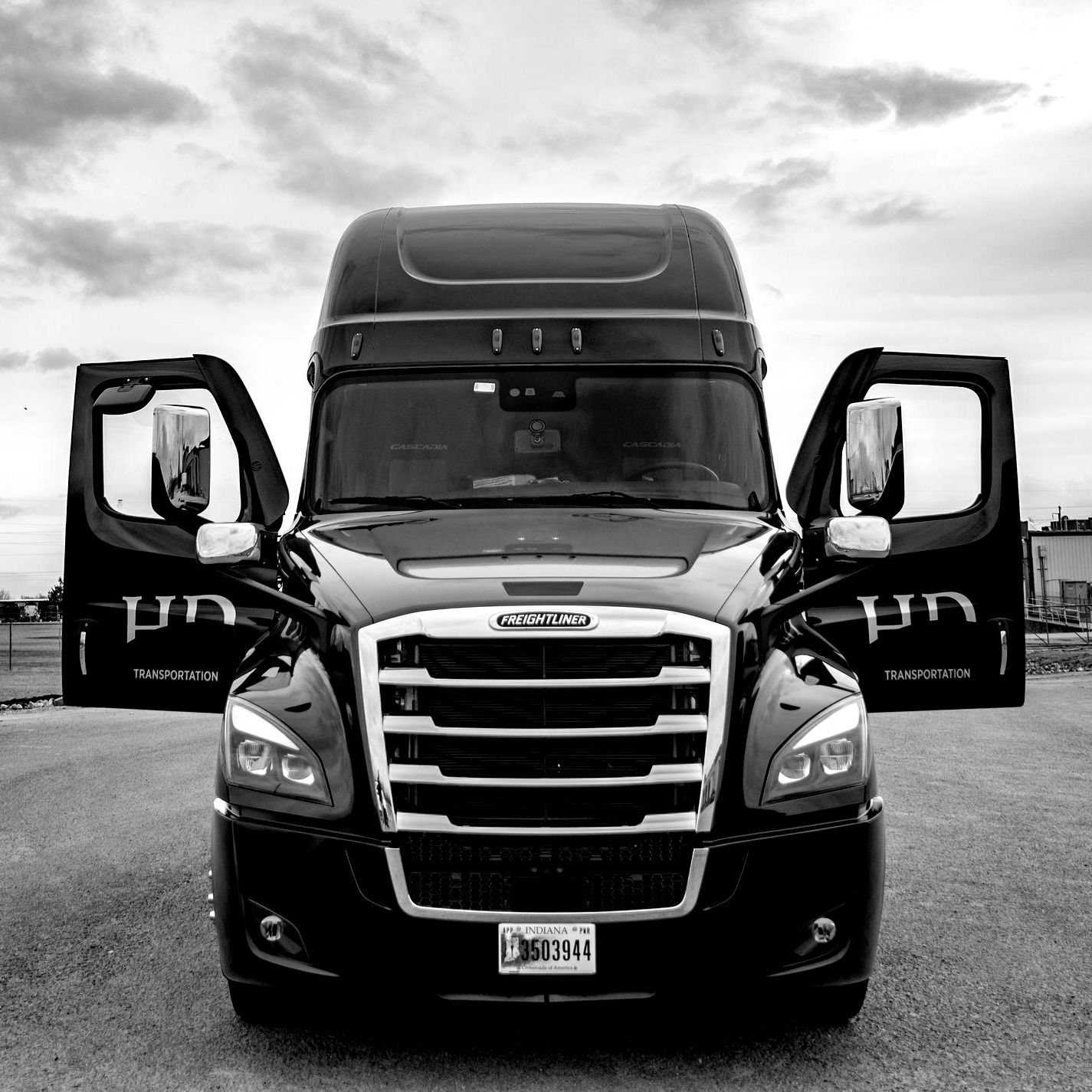 Black semi-truck with open doors parked outside on a cloudy day.