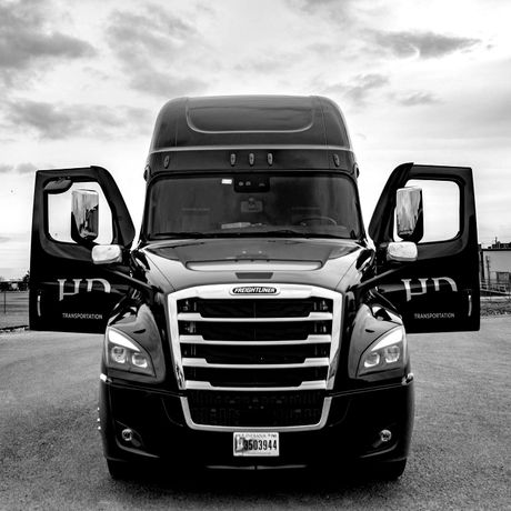 Black semi-truck with open doors parked outside on a cloudy day.