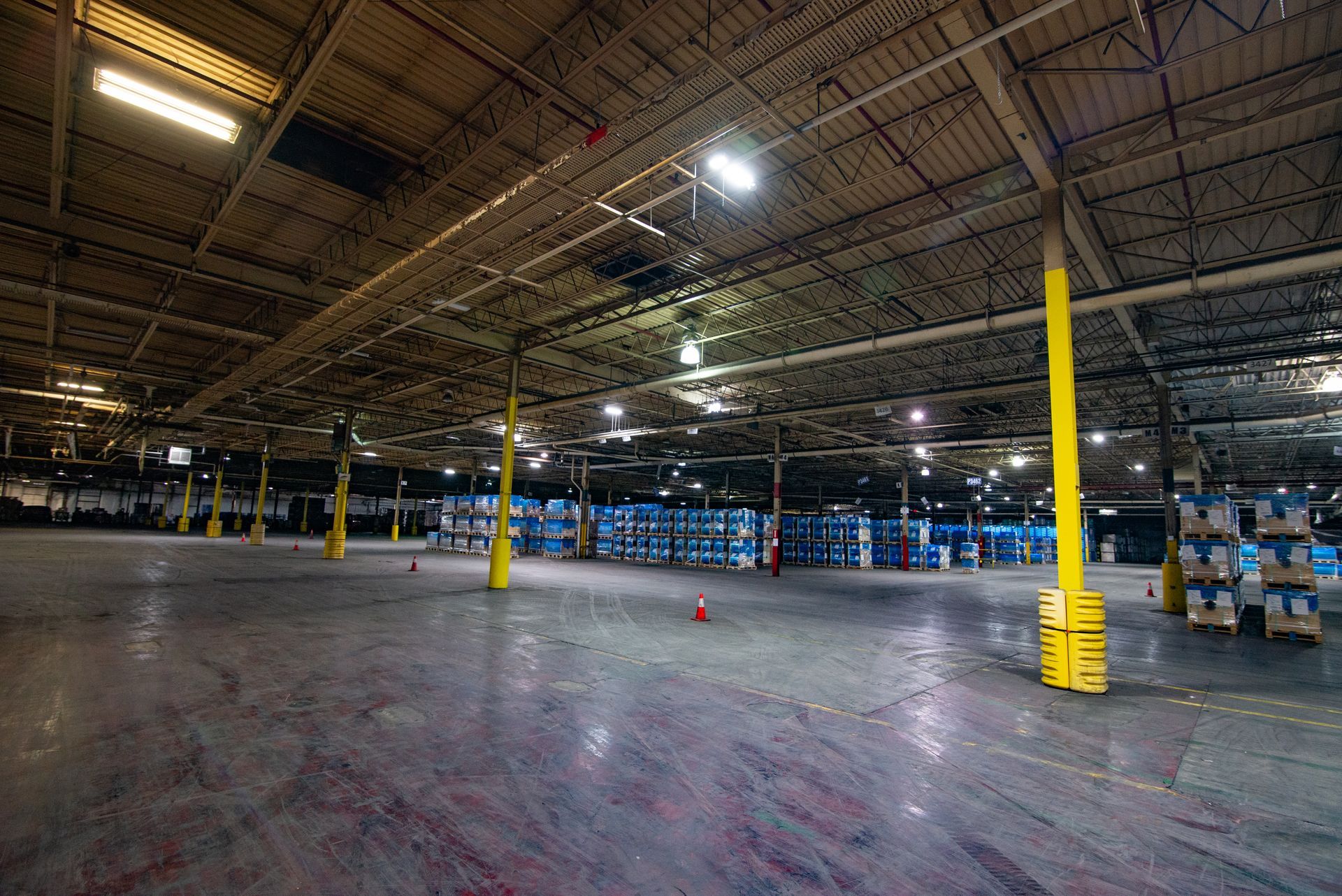 Large empty warehouse with blue water bottles stacked in the background; yellow support beams.