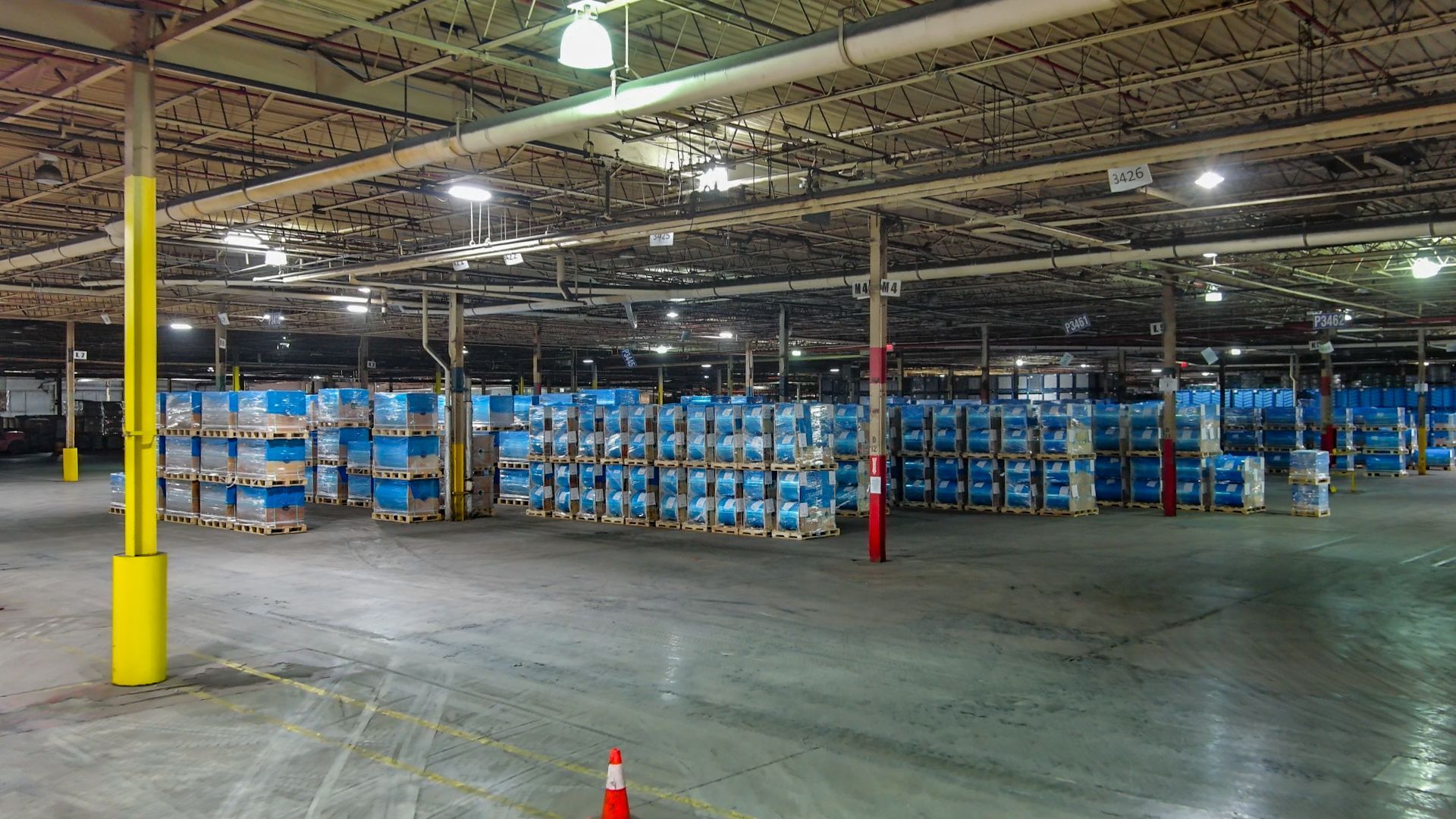 Warehouse interior with stacks of blue containers on pallets, metal support beams, and concrete floor.