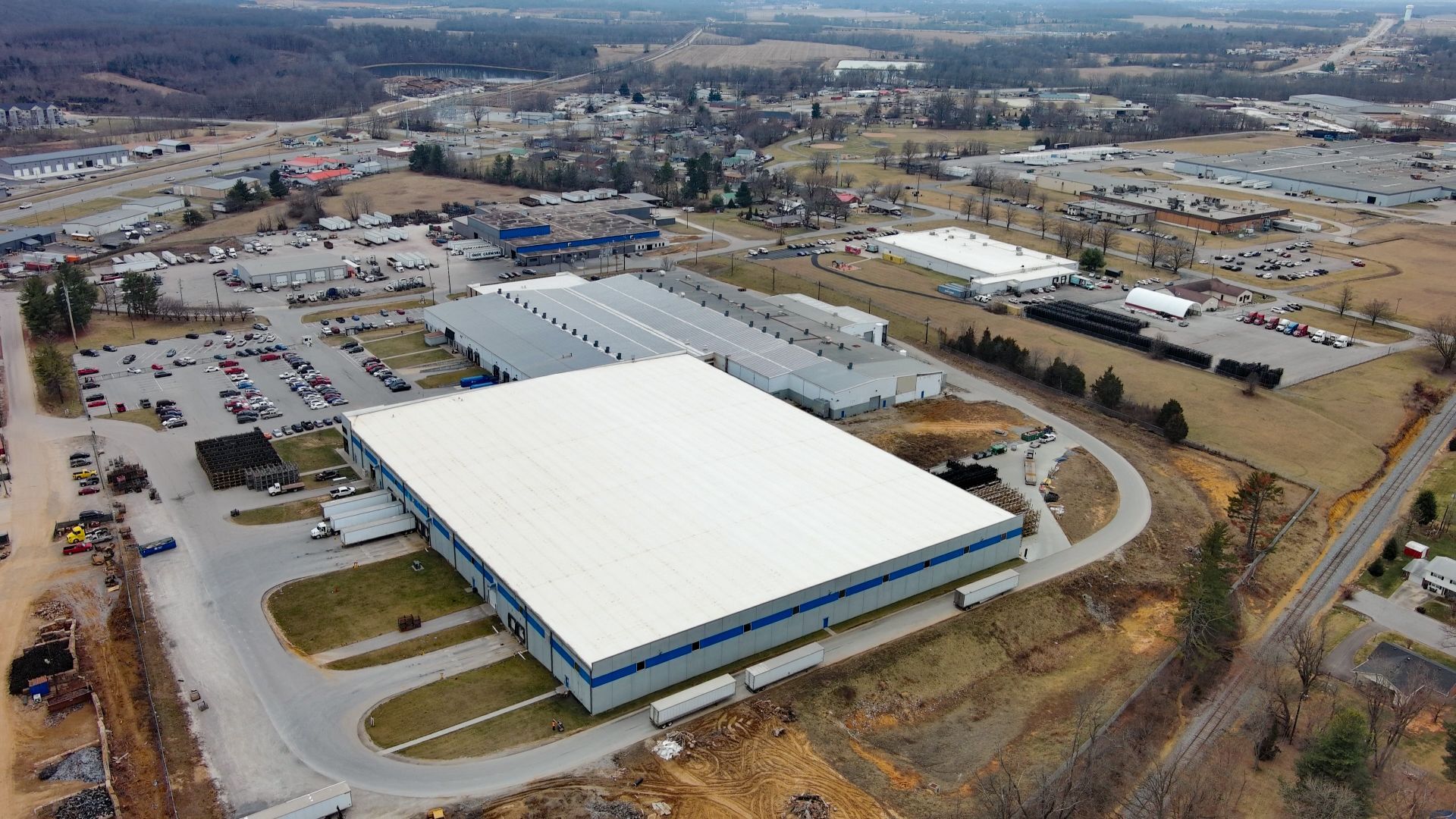 Aerial view of large industrial complex with several buildings, parking lots, and surrounding landscape.