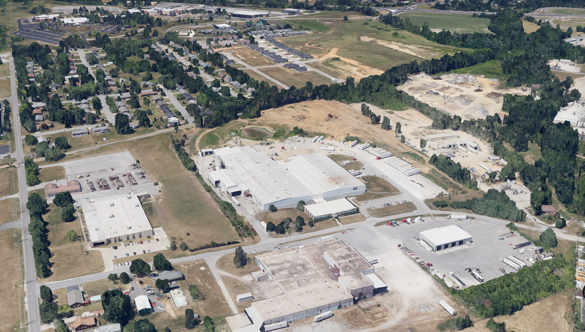 Aerial view of an industrial area with large buildings, parking lots, and a residential neighborhood in the background.