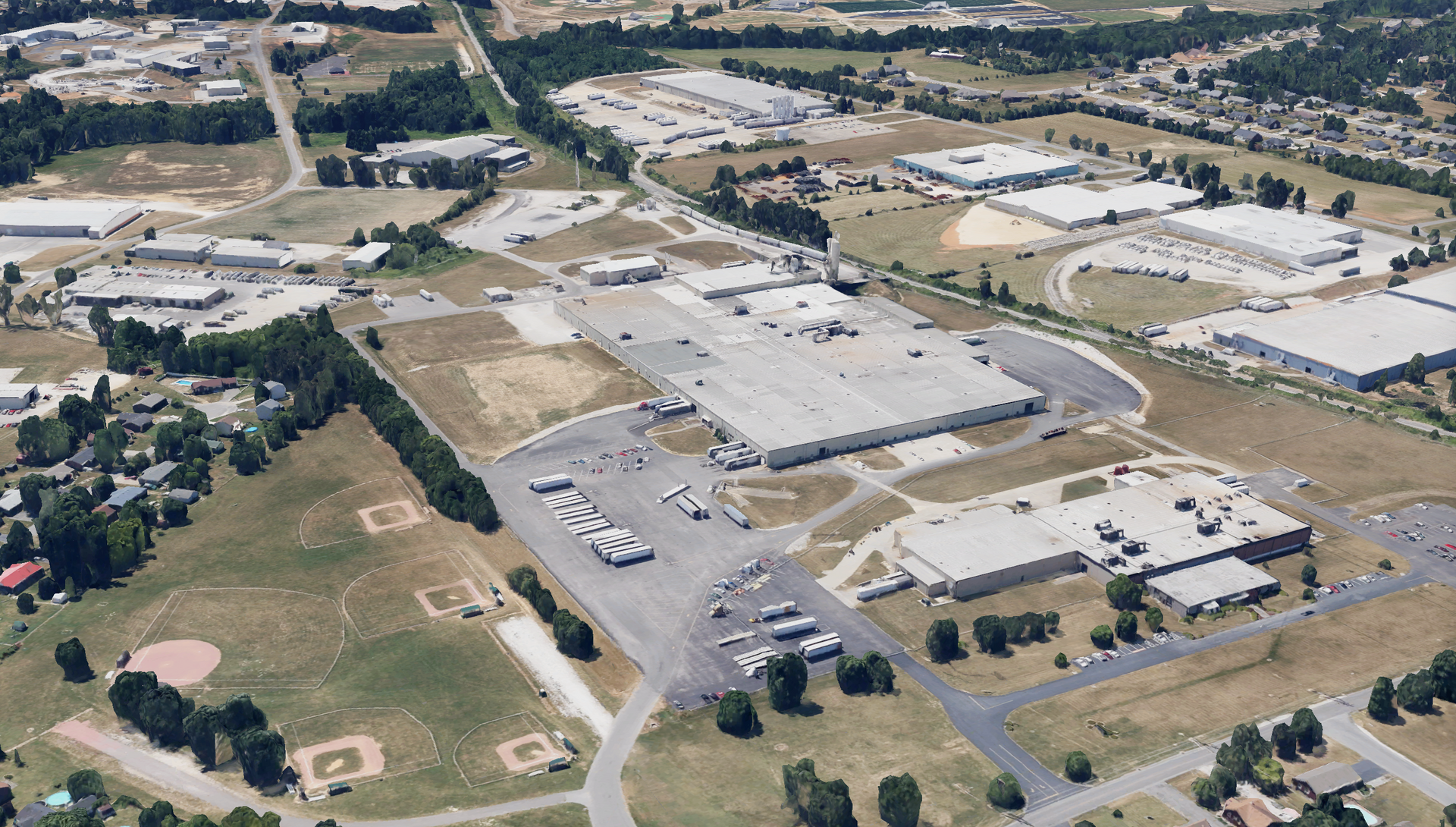 Aerial view of an industrial complex with large buildings, parking, and green spaces.