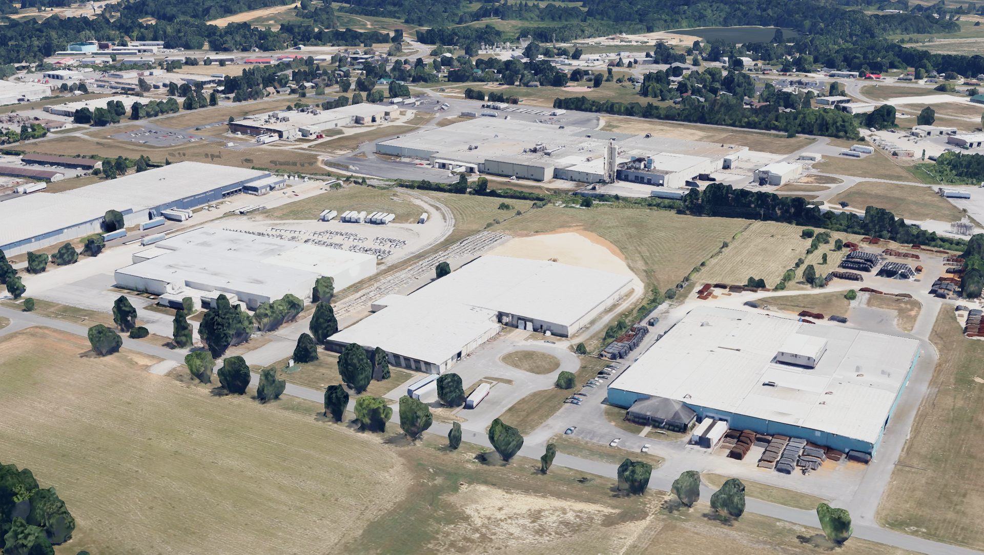 Aerial view of industrial park with large warehouse buildings, green fields, and surrounding trees.