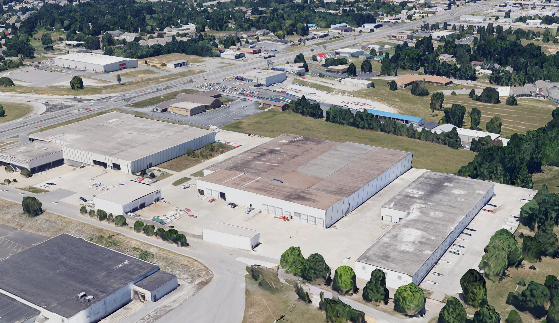 Aerial view of several industrial buildings in an open setting, with roads and other structures in the distance.