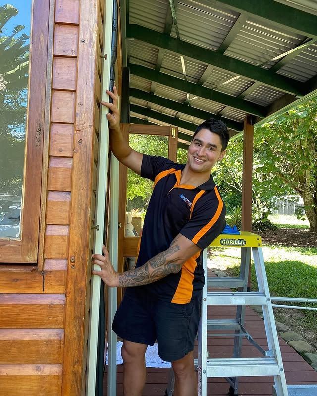 A Man Is Leaning Against a Wooden Wall Next to A Ladder — Recharged Air & Electrical in Innisfail, QLD