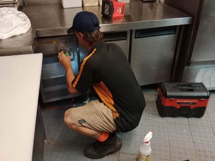 A Man Is Working on A Refrigerator in A Kitchen — Recharged Air & Electrical in Port Douglas, QLD