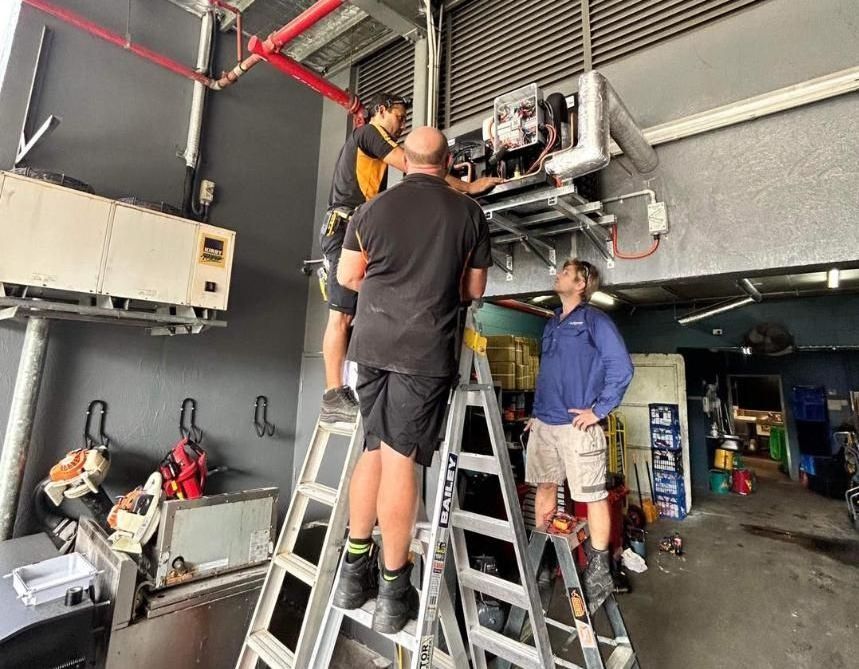 A Group of Men Are Working on A Machine in A Garage — Recharged Air & Electrical in Port Douglas, QLD