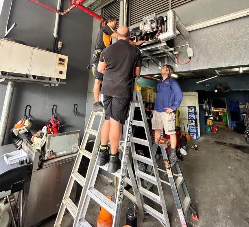 A Man Is Working on A Refrigerator in A Kitchen — Recharged Air & Electrical in Stratford, QLD