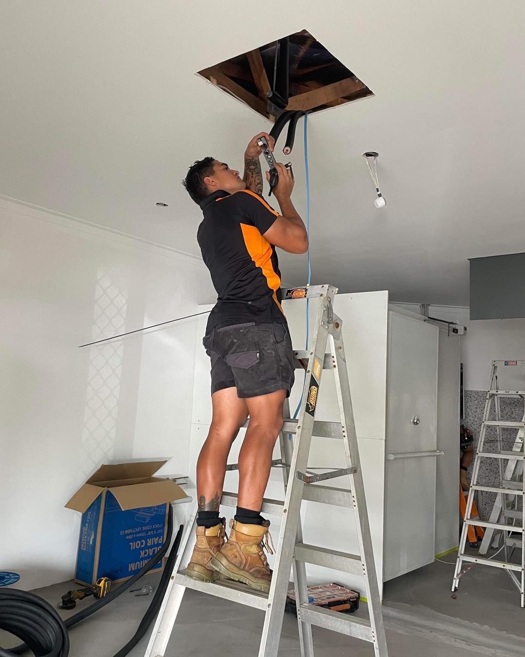 A Man Is Standing on A Ladder Working on A Ceiling — Recharged Air & Electrical in Stratford, QLD