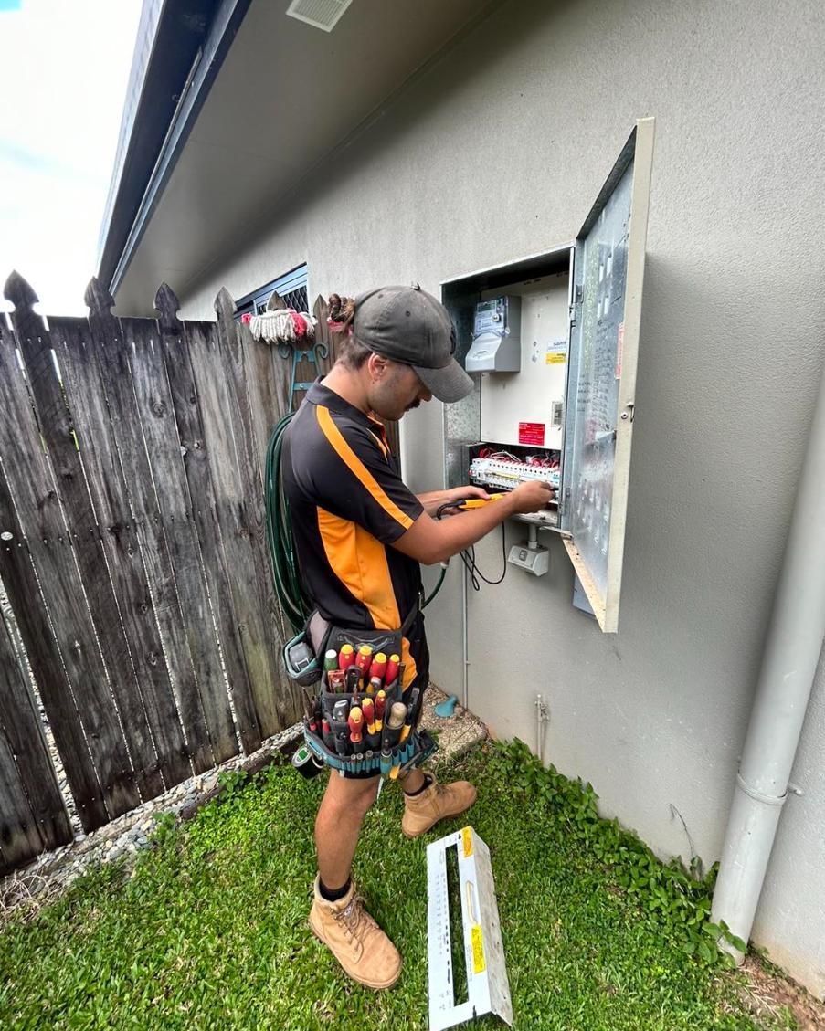 A Man Is Working on An Electrical Box Outside of A House — Recharged Air & Electrical in Gordonvale, QLD
