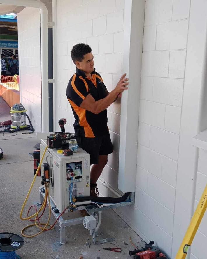 A Man Is Working on An Air Conditioner on A Wall — Recharged Air & Electrical in Cairns, QLD