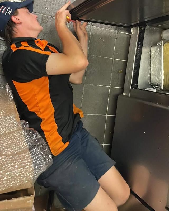 A Man in An Orange and Black Shirt Is Working on A Kitchen Counter — Recharged Air & Electrical in Mareeba, QLD