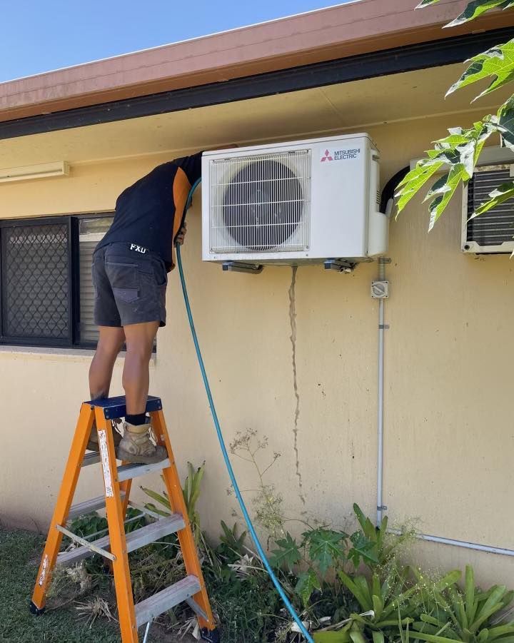 A Man Is Standing on A Ladder Next to An Air Conditioner — Recharged Air & Electrical in Stratford, QLD