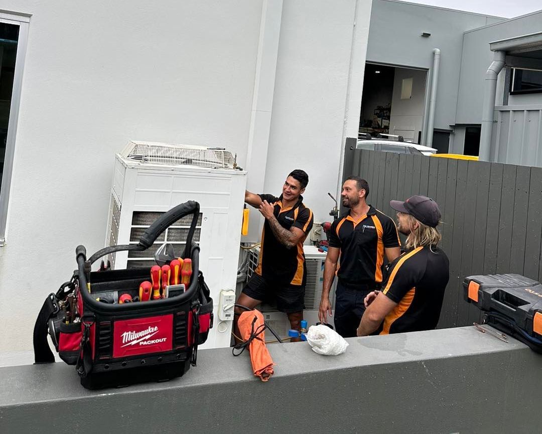 A Group of Men Are Working on An Air Conditioner Outside of A Building — Recharged Air & Electrical in Stratford, QLD