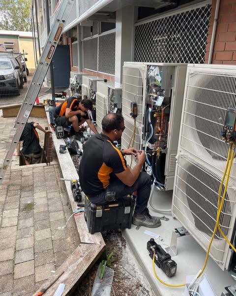 A Group of Men Are Working on An Air Conditioner Outside of A Building — Recharged Air & Electrical in Stratford, QLD