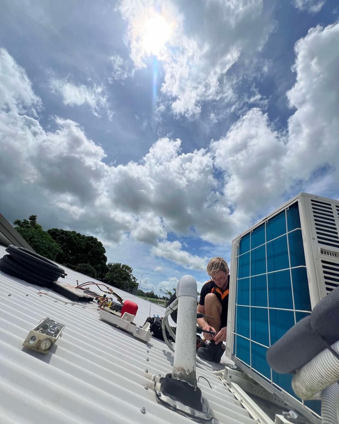 A Man Is Sitting on Top of A Roof Working on An Air Conditioner — Recharged Air & Electrical in Stratford, QLD