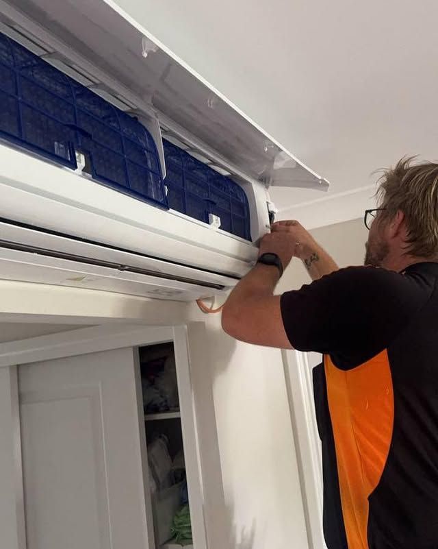 A Man Is Working on An Air Conditioner in A Room — Recharged Air & Electrical in Stratford, QLD