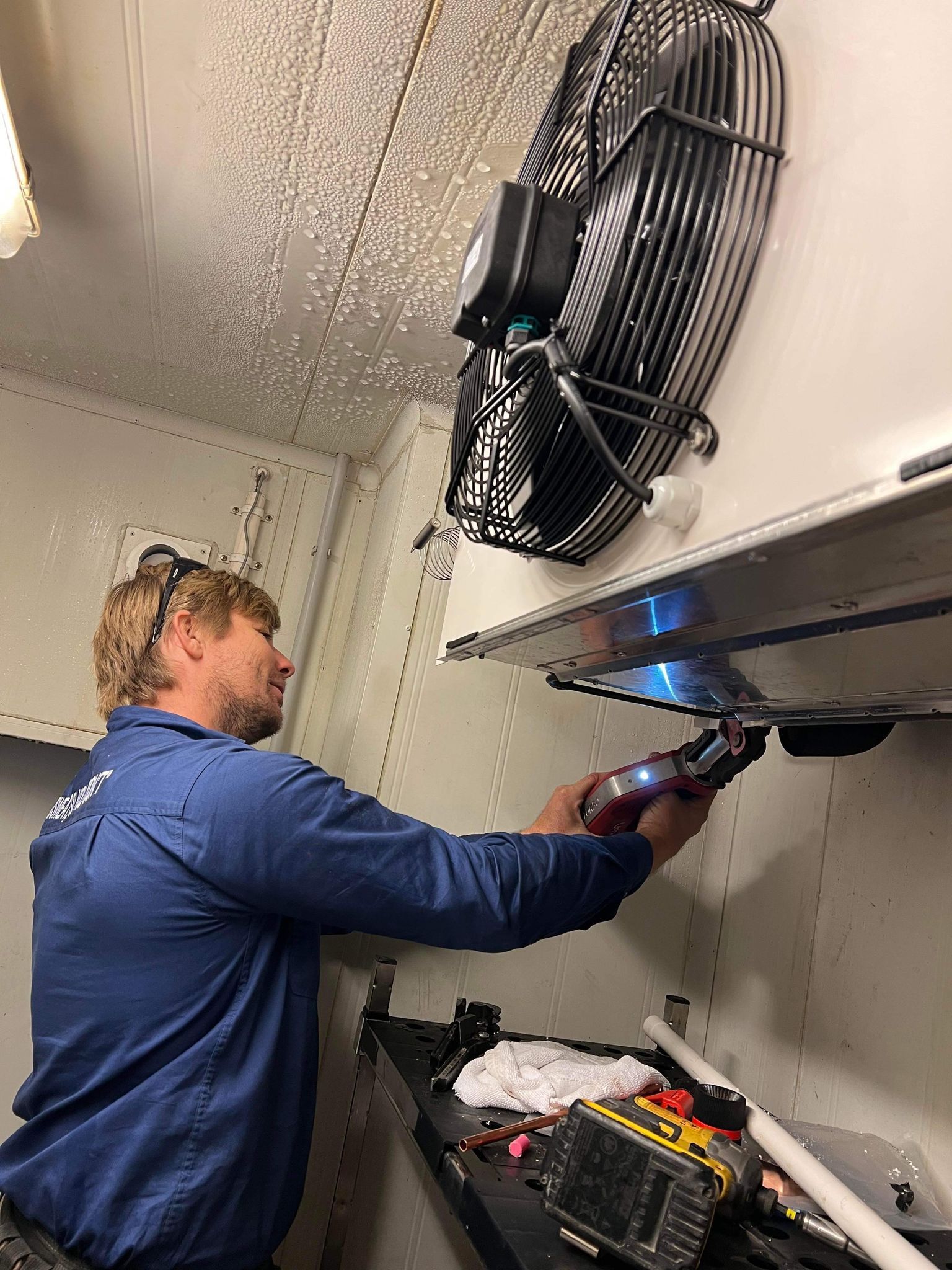 A Man in An Orange and Black Shirt Is Working on A Kitchen Counter — Recharged Air & Electrical in Stratford, QLD