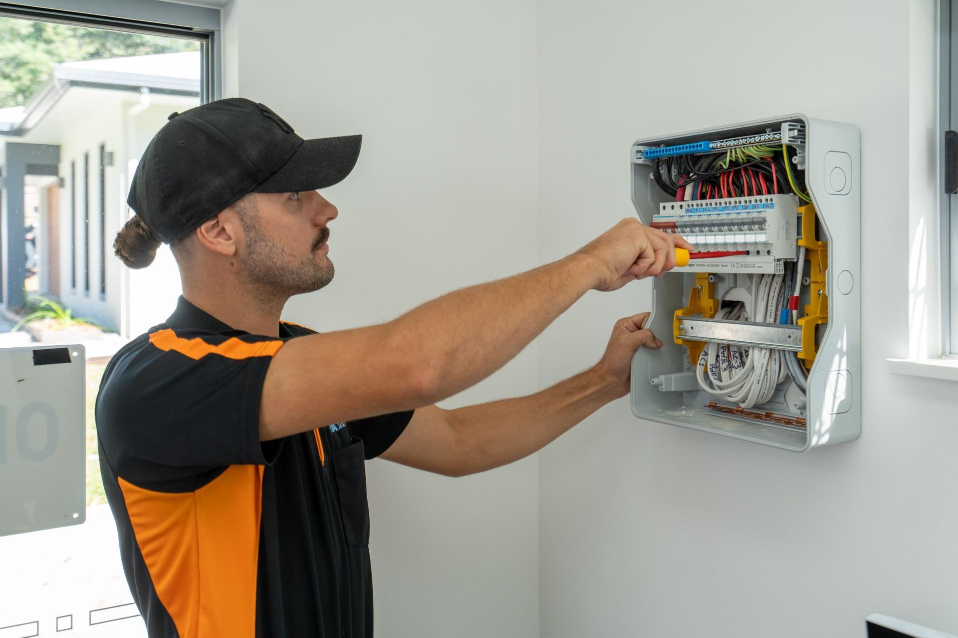 A Man Is Working on An Electrical Box on A Wall — Recharged Air & Electrical in Stratford, QLD