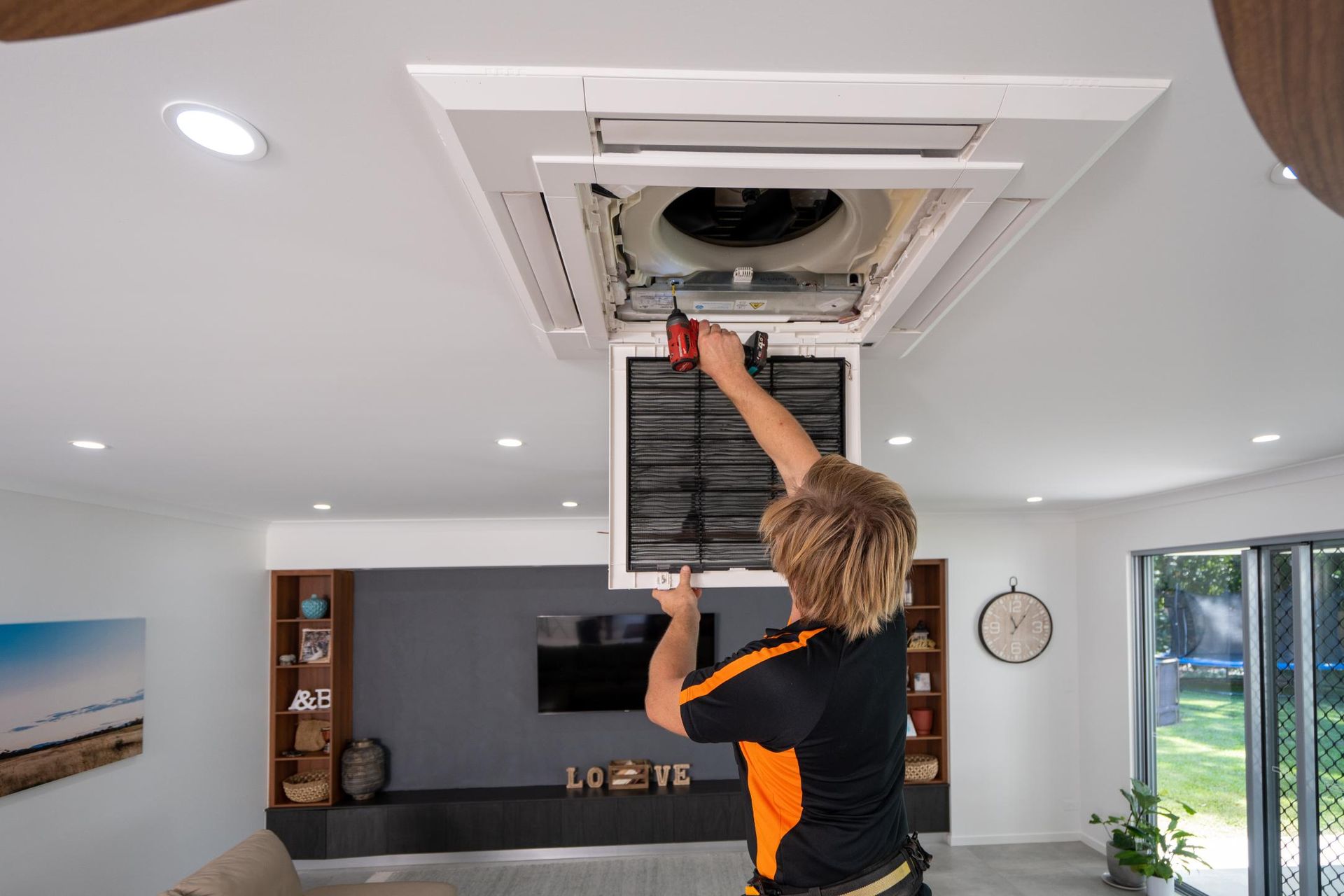 A Man Is Working on A Ceiling Fan in A Living Room — Recharged Air & Electrical in Stratford, QLD