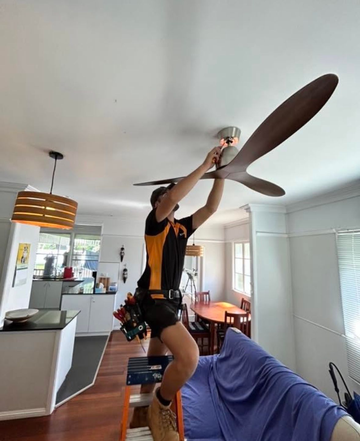 A Man Is Standing on A Ladder Working on A Ceiling Fan — Recharged Air & Electrical in Stratford, QLD